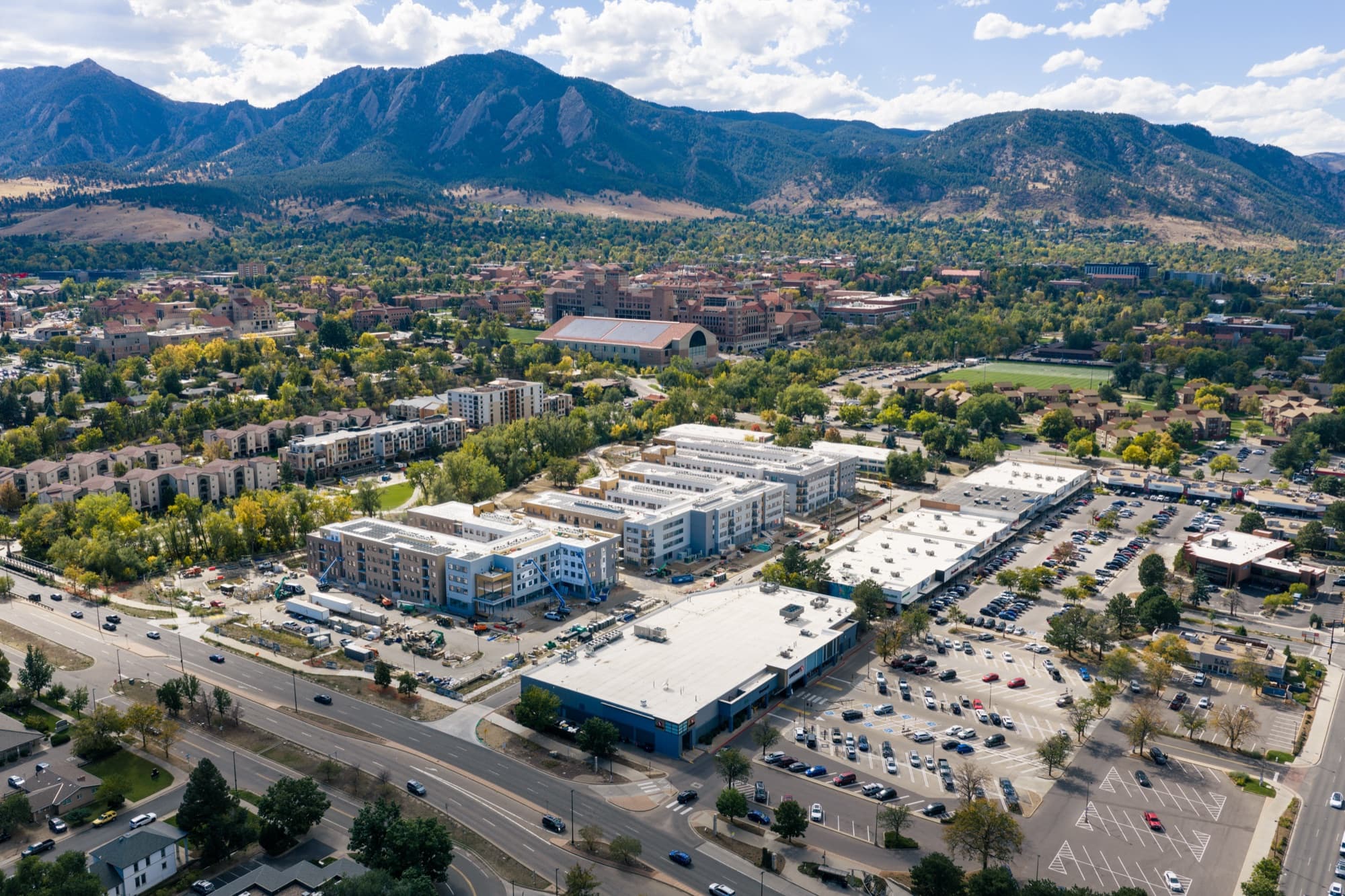 Drone photo of new apartment buildings in Boulder with CU campus and the Flatirons behind